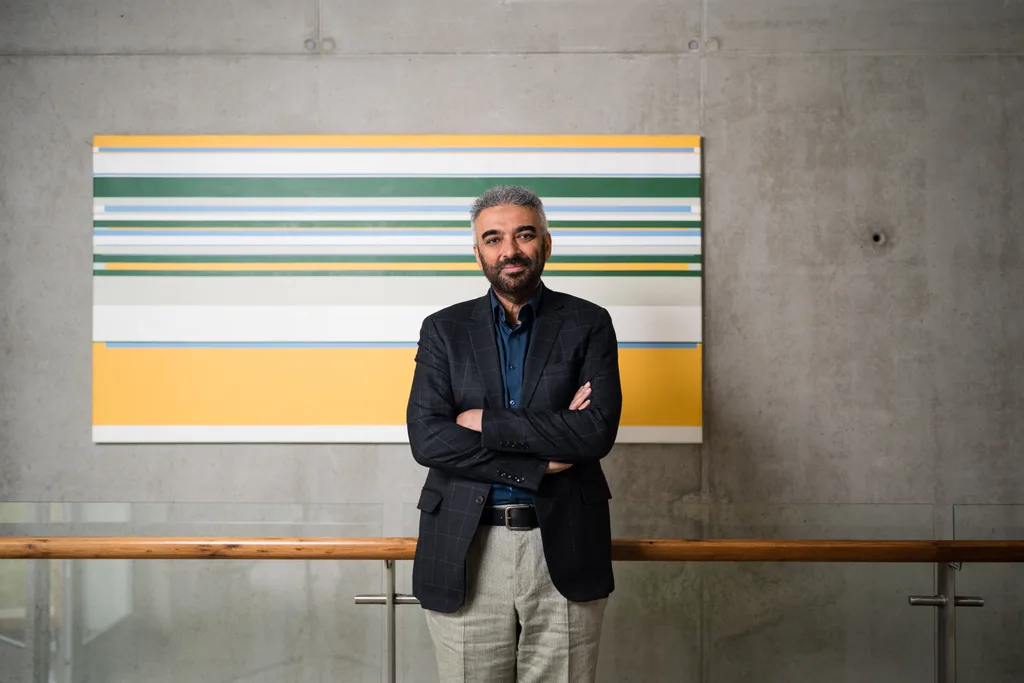 Aamir Malik, arms folded, standing in front of a large striped painting.